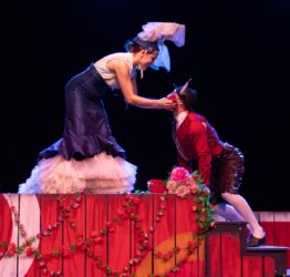 Two dancers, one leant over holding the others face, with a red flower in her hand.